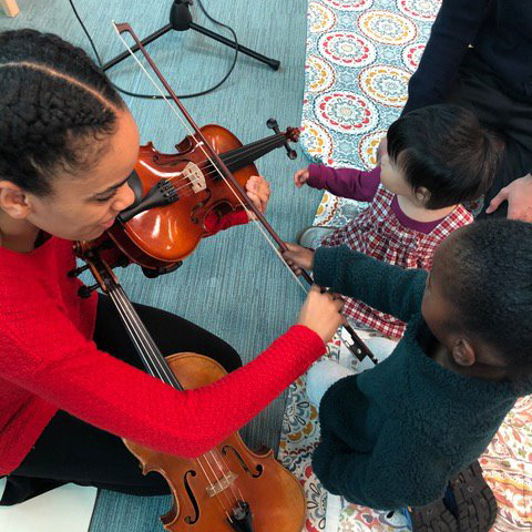 student playing violin for two children as a part of a BTC experience