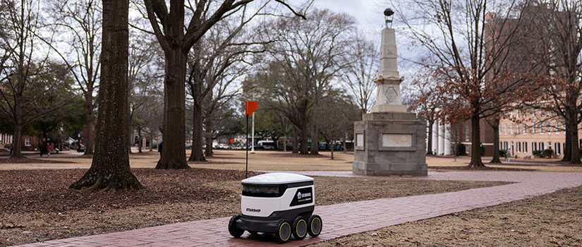 A Starship robot with a Grubhub logo on the side rolling near the Maxcy Monument on the Horseshoe