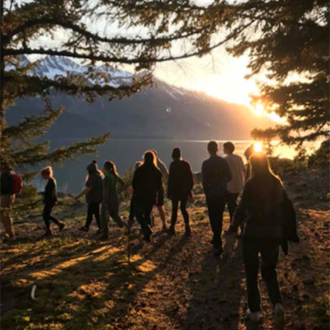 Students hike on mountain during golden hour. The mountain and a body of water are seen in the background. 