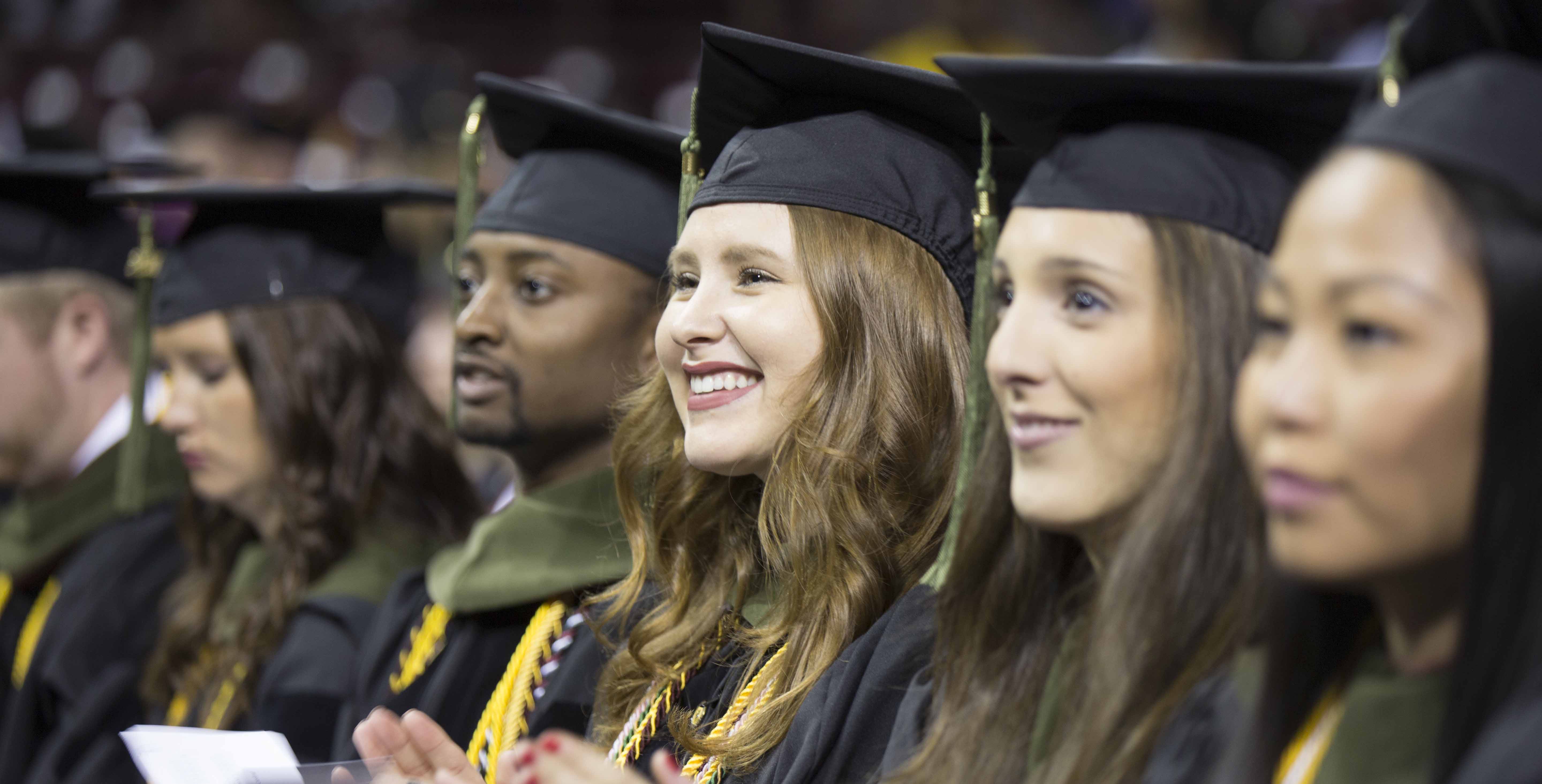 students sitting at commencement ceremony wearing black caps and gowns