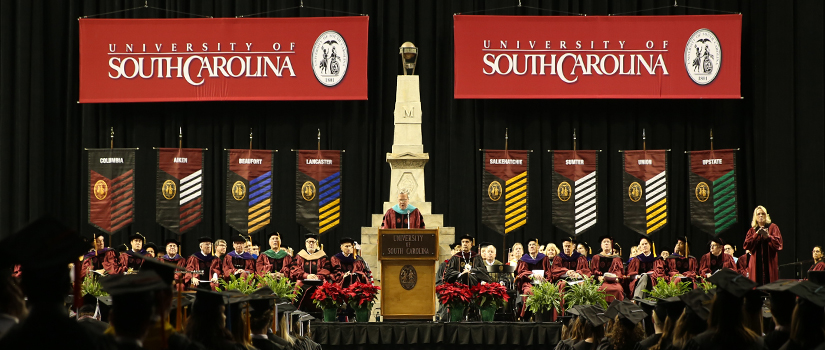 Commencement speaker in front of system banners.