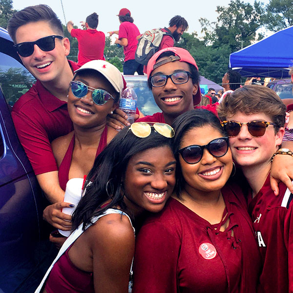 Students gathered together smiling at the camera wearing garnet and black gamecock gear at a tailgate.