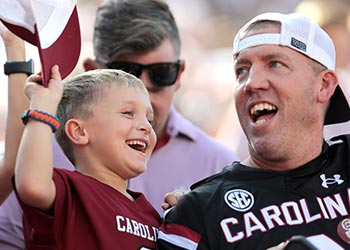 Dad and son wearing Gamecock jerseys cheering at a football game.