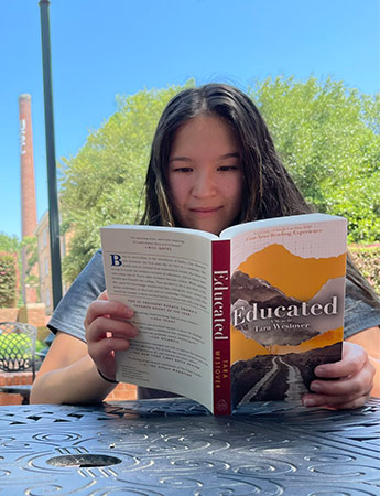 Student at an outdoor table reading the First-Year Reading Experience book 