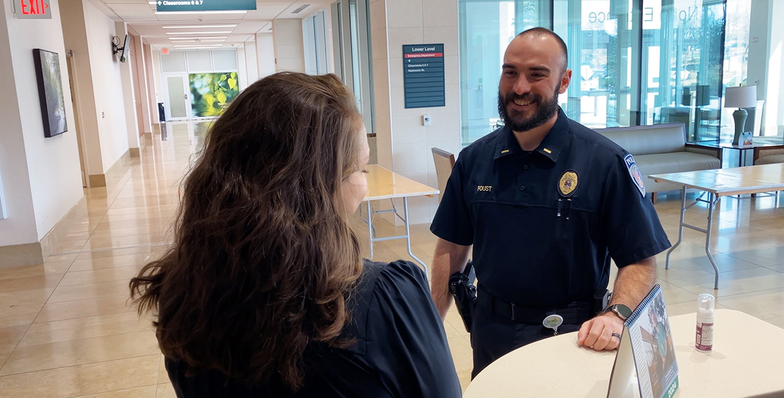 security officer with dark hair and beard talking to a woman in the hospital