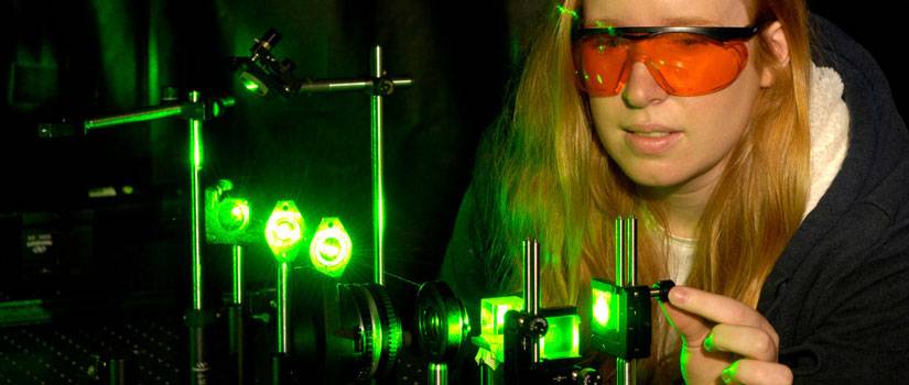 Female student in front of a green laser set up. 
