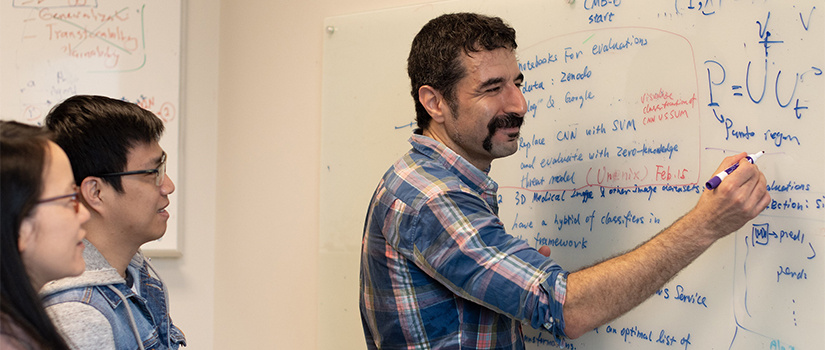 Dr. Jamshidi works with two grad students at a whiteboard