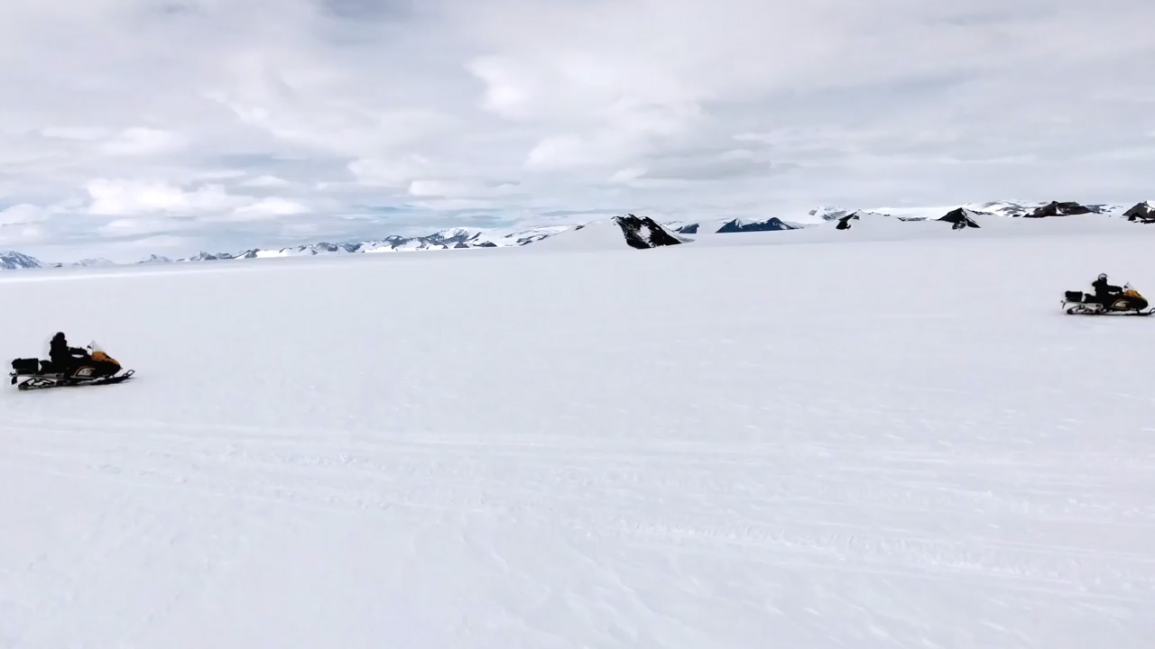 People riding in skidoos across the snow in Antarctica