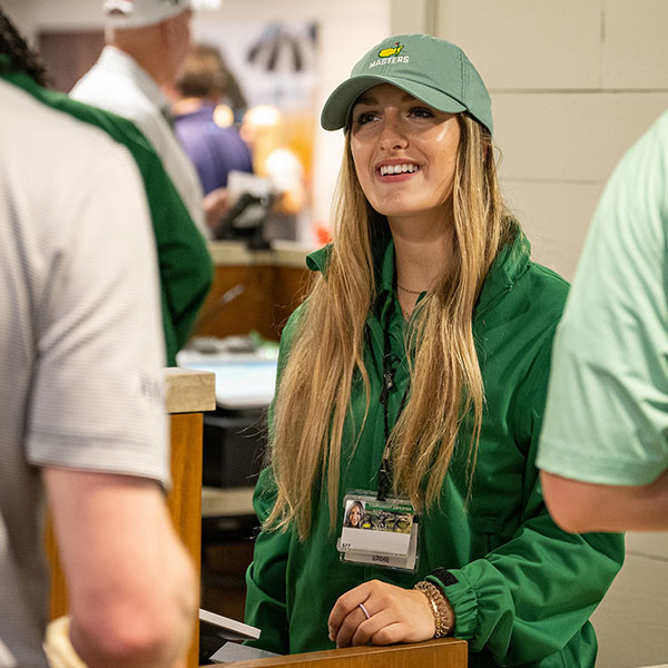 Student wearing Masters gear talking to customers at the Masters.