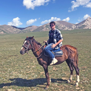 Josh Hughes sits on a horse with mountains in the background in Kyrgyzstan
