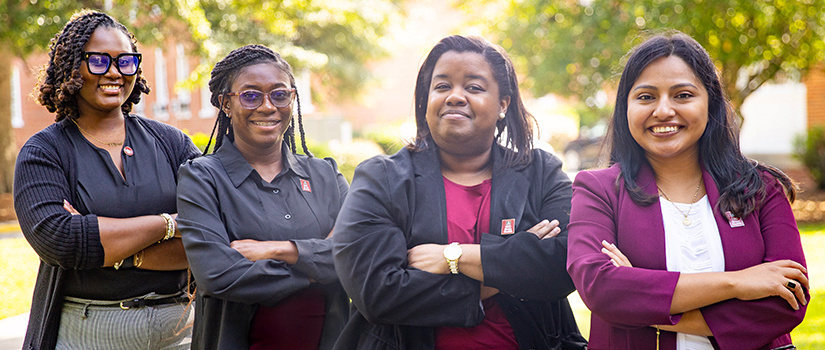 A group of four employees smiling for the camera outdoors. 