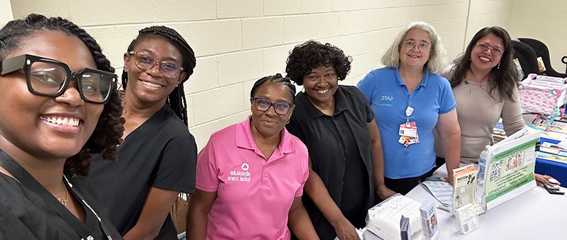 Image of a several woman leaning standing behind a table smiling for the camera.. 