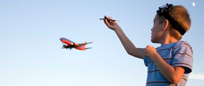 Boy holding model plane with real plane flying in background