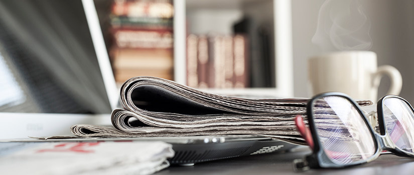 Glasses and newspaper on desk with computer.