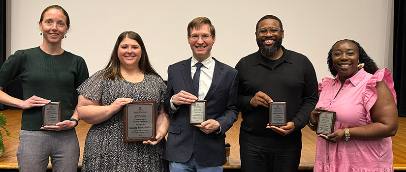 5 award winners stand side by side holding their award in front of them. Left to right are pictured a white female, white female, white male, black male, and black female. All are smiling at the camera. 
