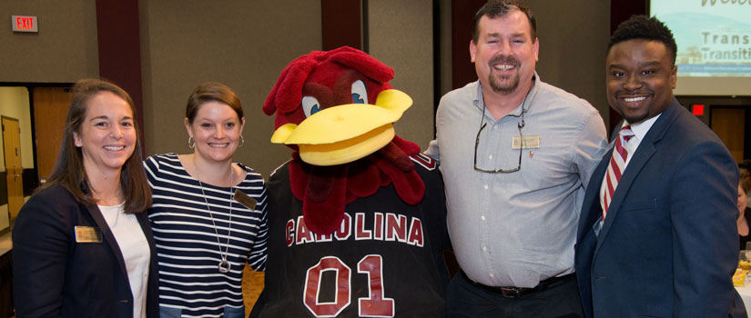 Four academic advisors are pictured with Cocky. Everyone is smiling. 