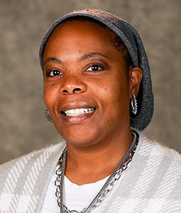 Shannon is pictured from the shoulders up wearing a gray sweater. She has dark skin and is smiling. 
