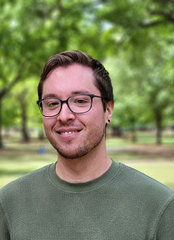 Jess is picture from the shoulders up wearing a green shirt. He has brown hair, is wearing glasses, and is smiling. 