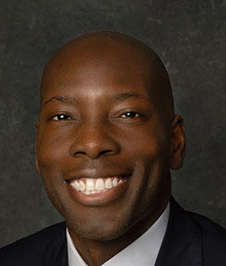 William is pictured from the shoulders up. He has dark skin and is smiling. 