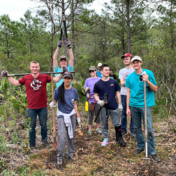 group of students standing in a forest, holding gardening tools