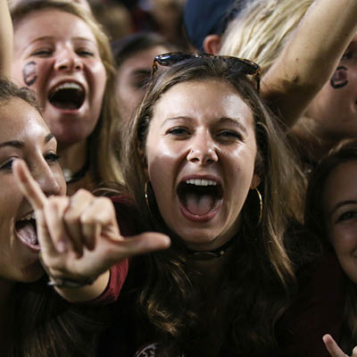 A close up of a student cheering with other students and their spurs raised.