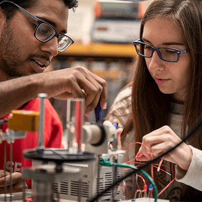 Two students adjusting wires on an object in a lab.