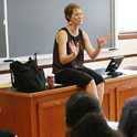 Female Professor lecturing while sitting on desk