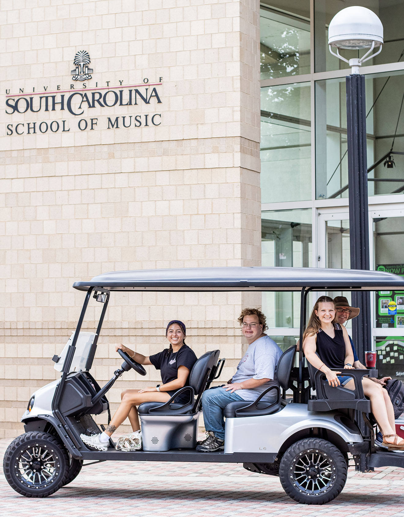 Students with disabilities ride in a golf cart in front of the University of South Carolina School of Music building.