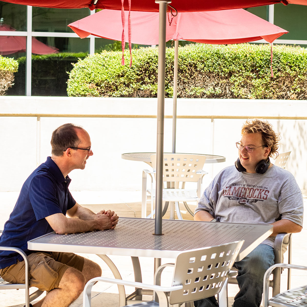 A staff member leans over a courtyard table to speak with a student.