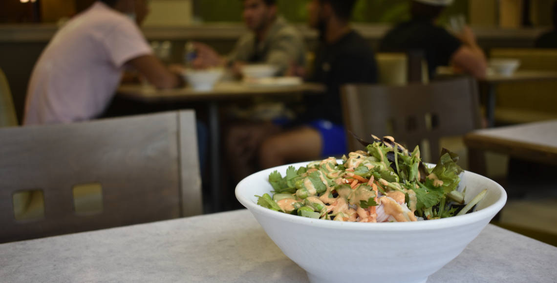 Poke bowl on a table with students dining in the background