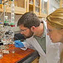 Two researchers in lab coats looking at glass beakers.