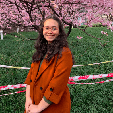 Girl with glasses standing and posing in front of a tree of pink flowers