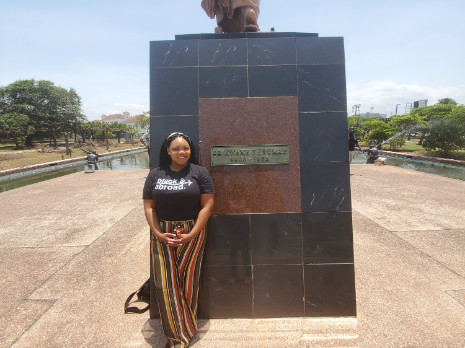 A Black woman wearing striped pants stands in front of a statue.