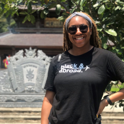 Black student wearing sunglasses smiles in front of a lake