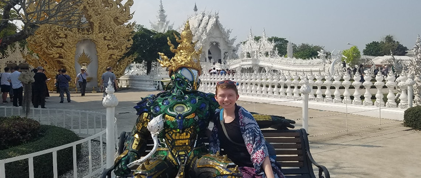 Woman sits in front of a Thai temple next to a robotic figure