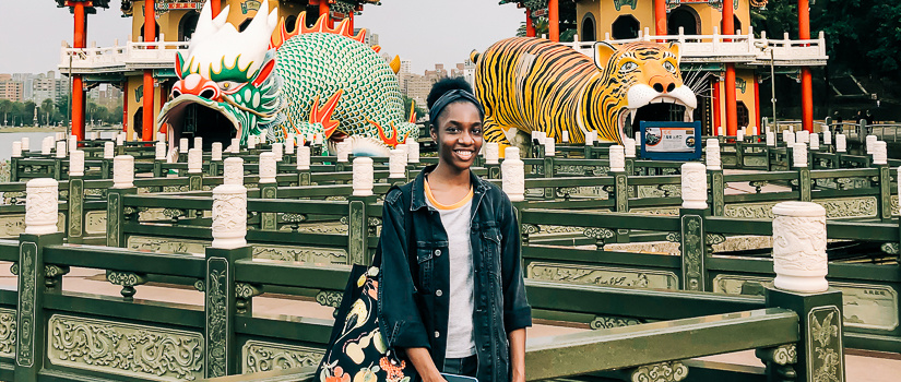 Tamera Sullivan standing in front of two traditional Taiwanese temples. On the left is a statue of a dragon. On the right is a statue of a tiger.