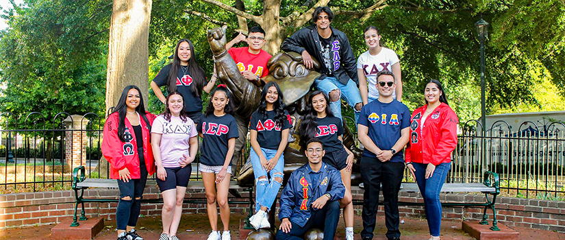 Greek students wearing their letters pose in front of the cocky statue.