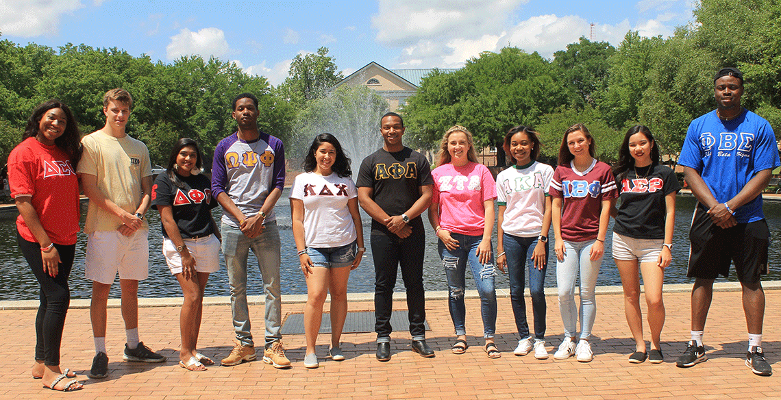 students in greek letter shirts pose in front of the library fountain