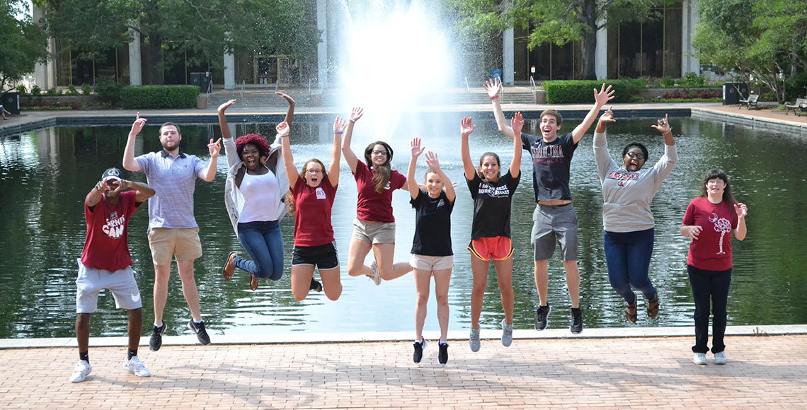 Gamecock Gateway orientation leaders leap into the air in front of the Thomas Cooper Library fountain.