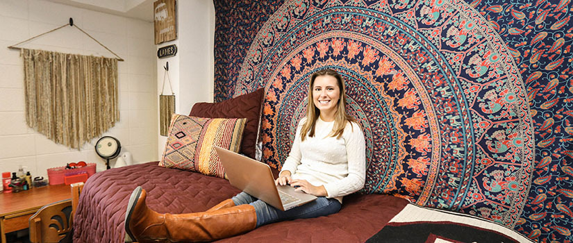 Gamecock Gateway student sits on her dorm room bed with her laptop