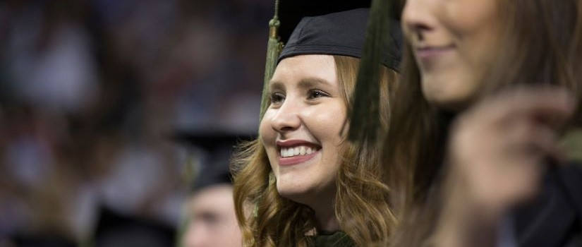 Close up a female's face, smiling with a graduate cap on, sitting in the UofSC graduation ceremony.