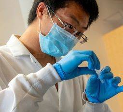 Faculty member wearing mask, gloves and lab coat, holding a test tube