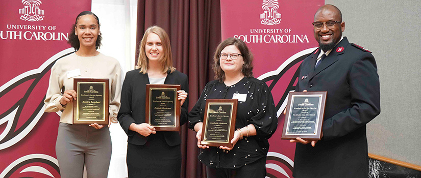 award winners pose in front of a UofSC banners. They hold their awards in their hands.
