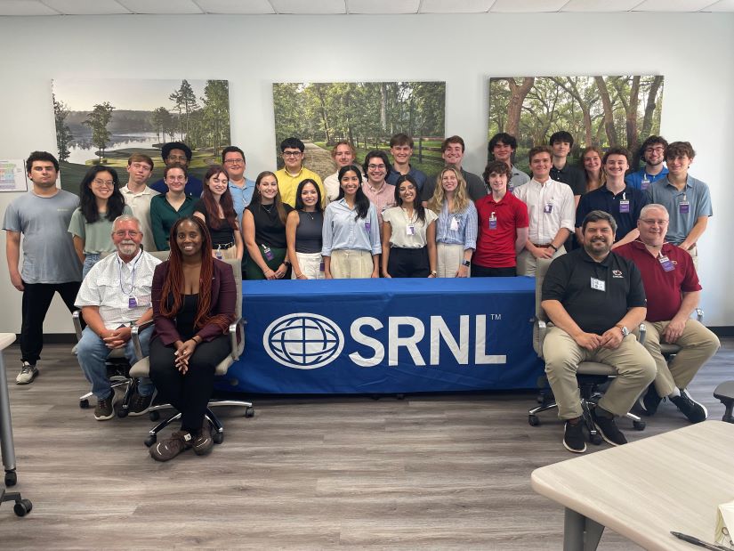 Students and staff posing around an SRNL table.