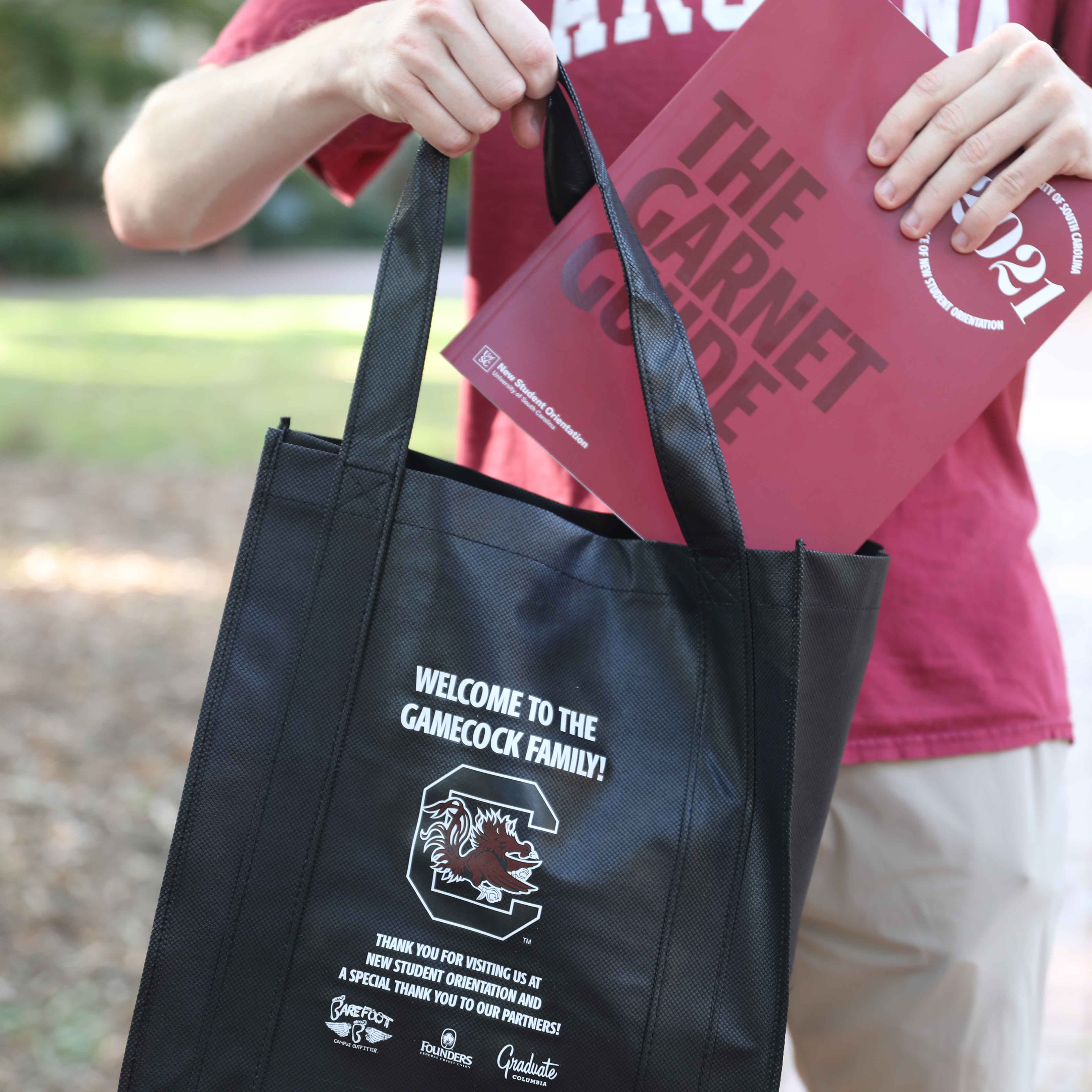 student holdind a copy of the Garnet Guide and a bag with corporate partner logos.