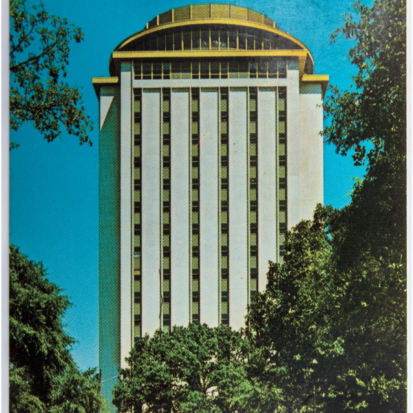 A vintage color postcard showing the University of South Carolina’s Capstone House, a tall white building with a distinctive gold-domed roof surrounded by trees and parked cars.