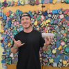 Adam stands in front of a colorful wall covered with messages and decorations.