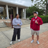 Two students stand outside a campus building and participate in an activity while engaging with one another.