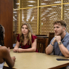 Two students sit at a table indoors and talk with another person during a campus event.