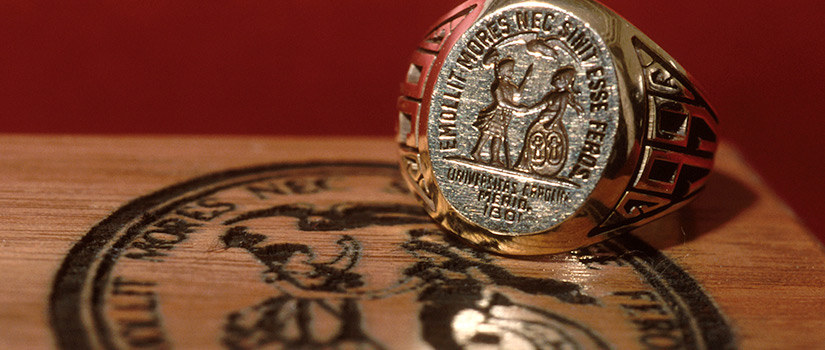 gold colored UofSC ring laying on a wooden table that has the university seal branded on the top